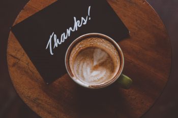 A cup of coffee next to a card that reads 'thanks'.